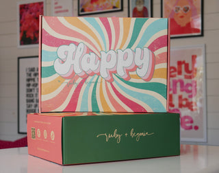 Colorful box with 'Happy' text on a white surface with framed pictures in the background